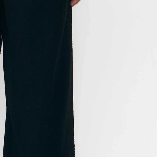 Pantalón de corte culotte en color negro con pernera ancha y corta, talle alto con cintura elástica y bolsillos laterales, fabricado en algodón orgánico.