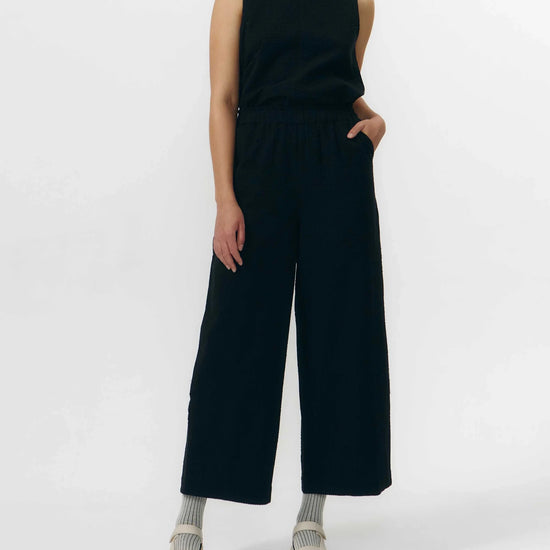 Pantalón de corte culotte en color negro con pernera ancha y corta, talle alto con cintura elástica y bolsillos laterales, fabricado en algodón orgánico.