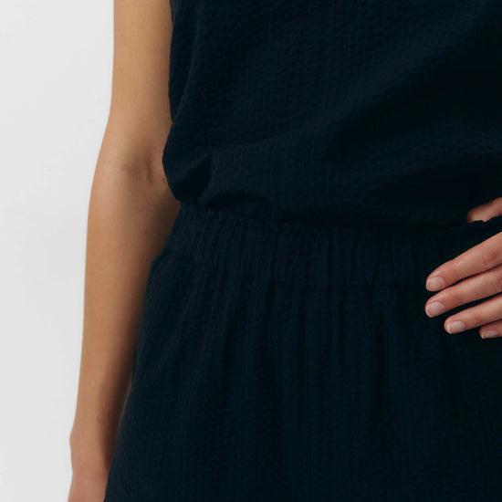 Pantalón de corte culotte en color negro con pernera ancha y corta, talle alto con cintura elástica y bolsillos laterales, fabricado en algodón orgánico.