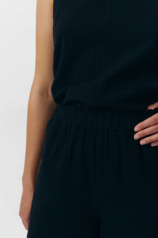 Pantalón de corte culotte en color negro con pernera ancha y corta, talle alto con cintura elástica y bolsillos laterales, fabricado en algodón orgánico.
