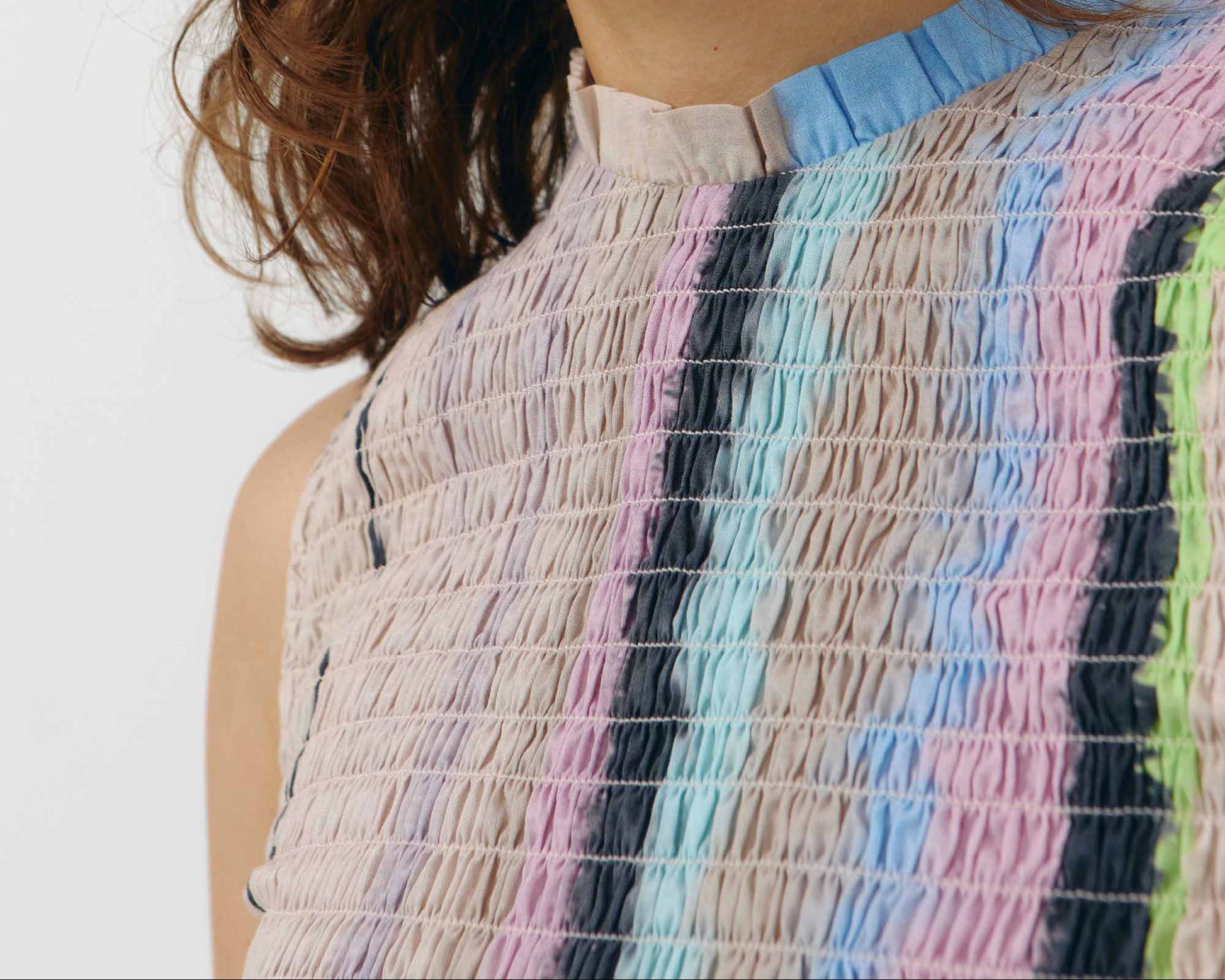 Top sin mangas de algodón orgánico con cuerpo elástico nido de abeja y cuello con volante, con un estampado artístico de ondas azules sobre fondo blanco.