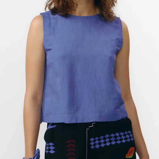 Top sin mangas de color azul medio con cuello redondo y cierre de botones naturales, con diseño reversible que permite llevar los botones en la parte frontal o trasera.