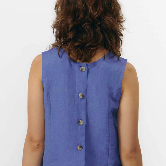 Top sin mangas de color azul medio con cuello redondo y cierre de botones naturales, con diseño reversible que permite llevar los botones en la parte frontal o trasera.