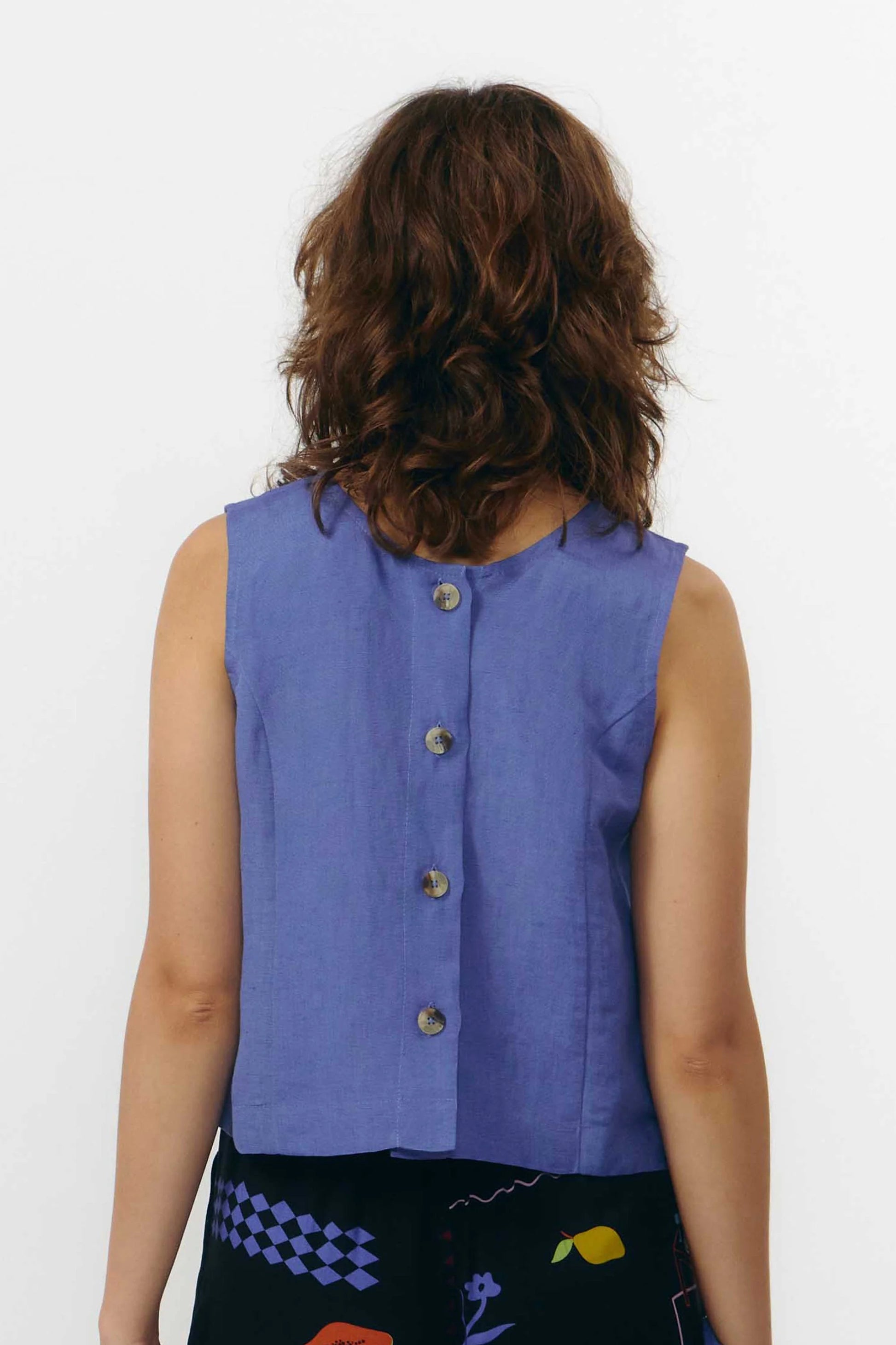 Top sin mangas de color azul medio con cuello redondo y cierre de botones naturales, con diseño reversible que permite llevar los botones en la parte frontal o trasera.
