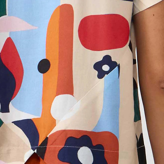 Camisa de manga corta con cuello de solapa y estampado artístico de barcos y motivos marineros en color azul sobre fondo crema, con botones de material natural.