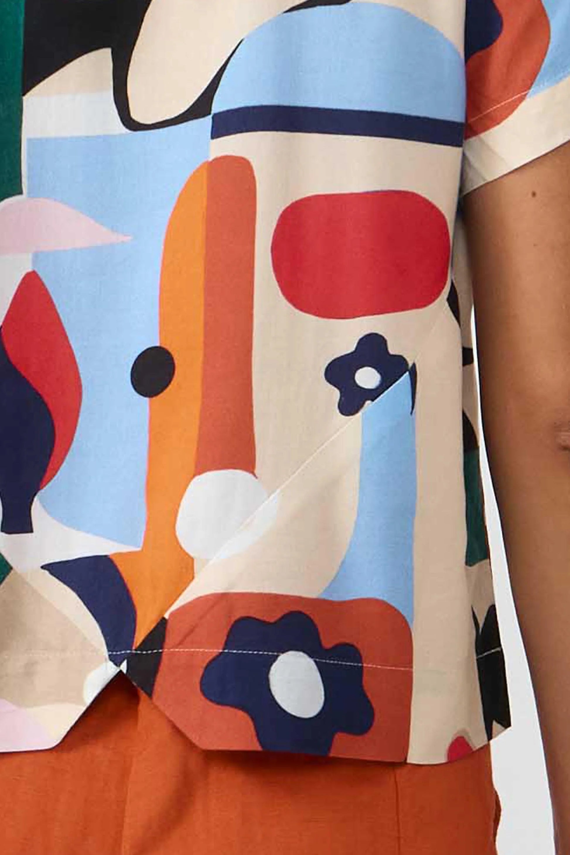 Camisa de manga corta con cuello de solapa y estampado artístico de barcos y motivos marineros en color azul sobre fondo crema, con botones de material natural.