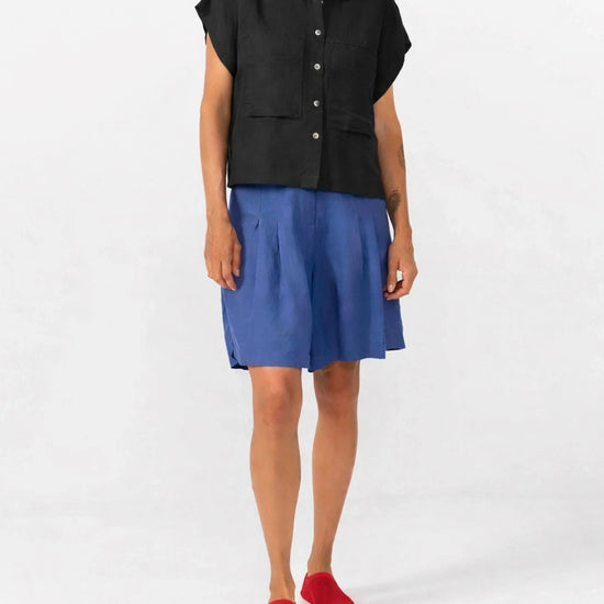 Camisa de manga corta en color negro con caída fluida, confeccionada en mezcla de lino y viscosa sostenible, con cuello clásico y botones frontales de tono natural.