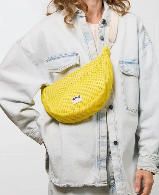 Bolso bandolera de color amarillo en tejido de rejilla (mesh) con correa cruzada ajustable de algodón, cremallera superior y etiqueta frontal de silicona, modelo Ray de Wouf.