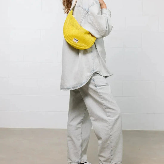 Bolso bandolera de color amarillo en tejido de rejilla (mesh) con correa cruzada ajustable de algodón, cremallera superior y etiqueta frontal de silicona, modelo Ray de Wouf.