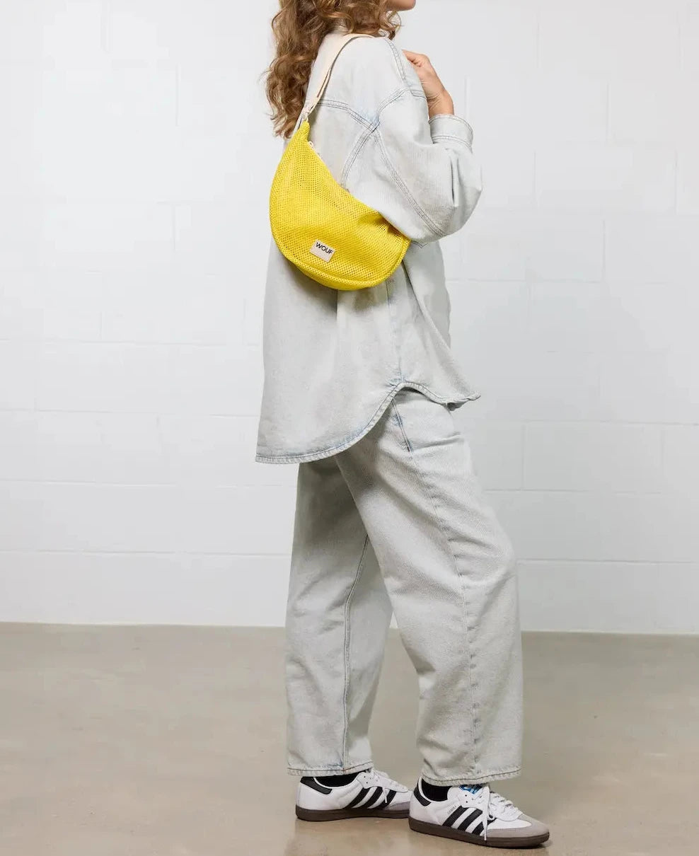 Bolso bandolera de color amarillo en tejido de rejilla (mesh) con correa cruzada ajustable de algodón, cremallera superior y etiqueta frontal de silicona, modelo Ray de Wouf.