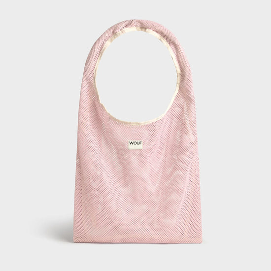 Bolso grande tipo camiseta de color rosa empolvado en tejido de rejilla (mesh) con asas integradas y etiqueta frontal de silicona, marca Wouf.