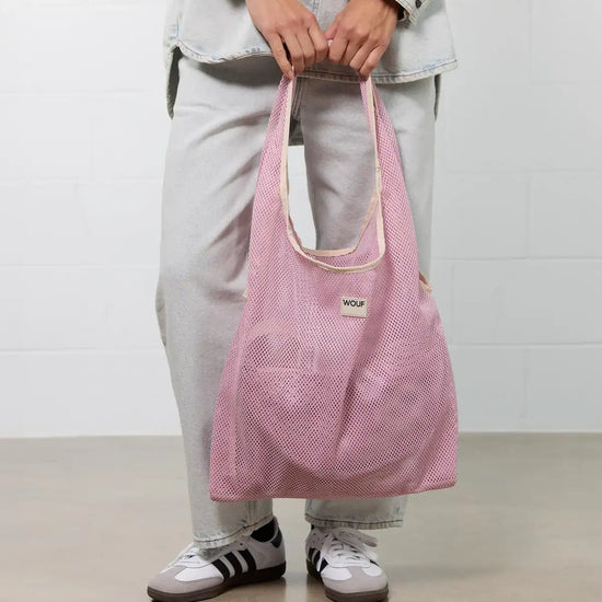 Bolso grande tipo camiseta de color rosa empolvado en tejido de rejilla (mesh) con asas integradas y etiqueta frontal de silicona, marca Wouf.
