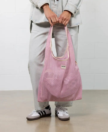 Bolso grande tipo camiseta de color rosa empolvado en tejido de rejilla (mesh) con asas integradas y etiqueta frontal de silicona, marca Wouf.