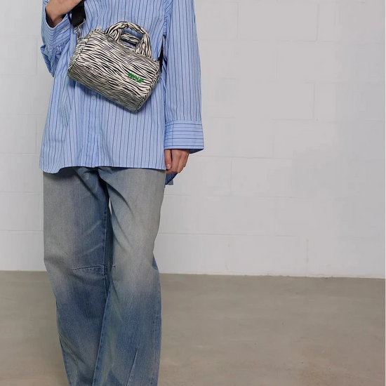 Bolso tipo bowling con estampado animal print de cebra, logo metálico frontal, asas cortas acolchadas y correa larga extraíble, modelo Zebra Hit de Wouf.