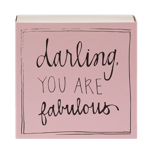 Caja de cerillas cuadrada de color rosa con el texto 'Darling you are fabulous' impreso, que contiene 125 cerillas largas de madera negra y punta blanca.