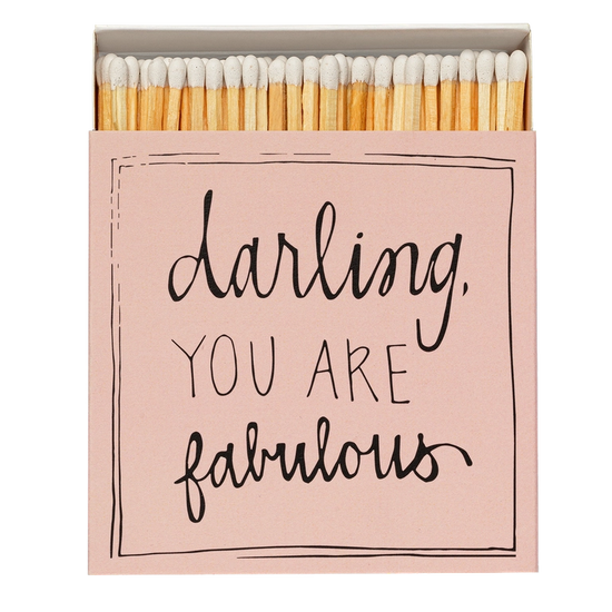 Caja de cerillas cuadrada de color rosa con el texto 'Darling you are fabulous' impreso, que contiene 125 cerillas largas de madera negra y punta blanca.
