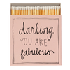 Caja de cerillas cuadrada de color rosa con el texto 'Darling you are fabulous' impreso, que contiene 125 cerillas largas de madera negra y punta blanca.