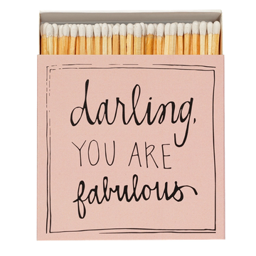 Caja de cerillas cuadrada de color rosa con el texto 'Darling you are fabulous' impreso, que contiene 125 cerillas largas de madera negra y punta blanca.