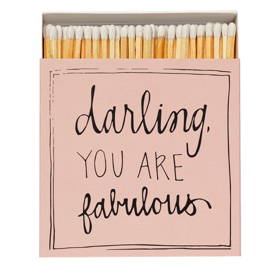 Caja de cerillas cuadrada de color rosa con el texto 'Darling you are fabulous' impreso, que contiene 125 cerillas largas de madera negra y punta blanca.