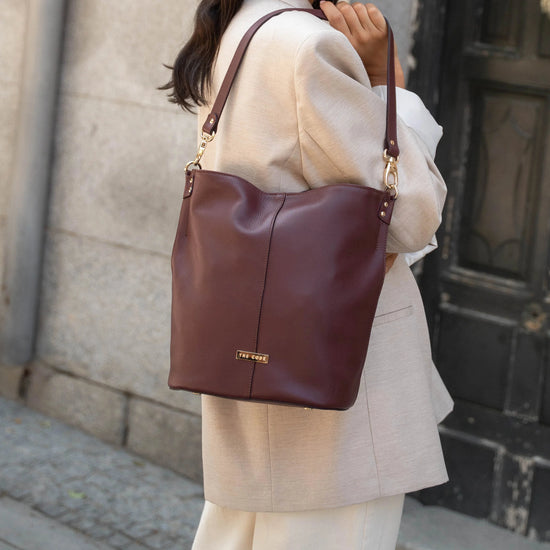 Bolso tipo bombonera de piel lisa color burdeos con asa corta de mano y bandolera ajustable, cierre de imán y fabricación artesanal española de The Code.