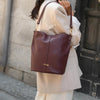 Bolso tipo bombonera de piel lisa color burdeos con asa corta de mano y bandolera ajustable, cierre de imán y fabricación artesanal española de The Code.